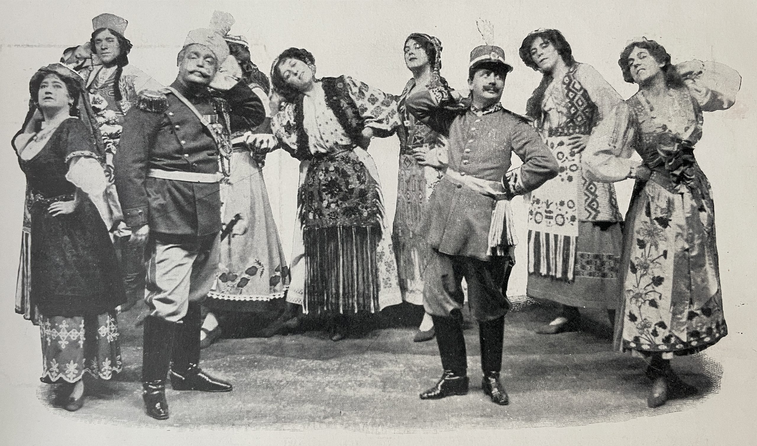 Two male late 19th century soldiers striking a comic pose (one hand behind head) with seven rurally dressed women behind striking the same pose. Scene from the Chocolate Solider, Lyric Theatre, UK, c.1910. Image from the Play Pictorial